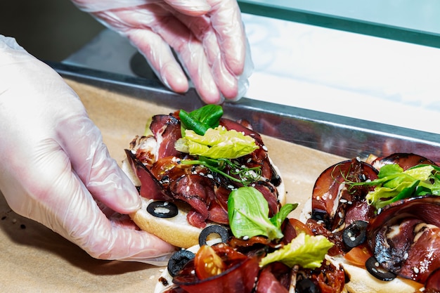 Las manos del camarero en guantes sostienen un sándwich con carne. Catering en eventos.