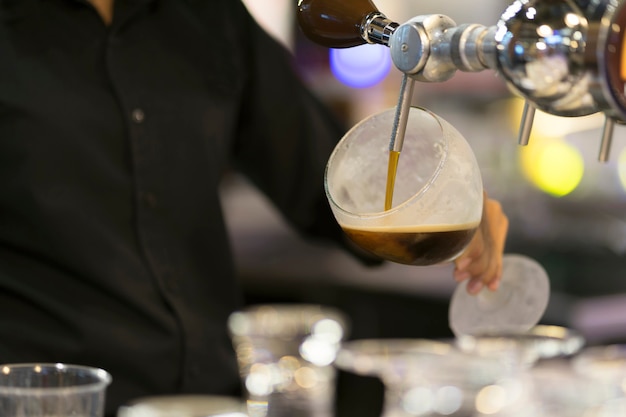 Foto manos del camarero que vierten una cerveza negra en un vidrio.