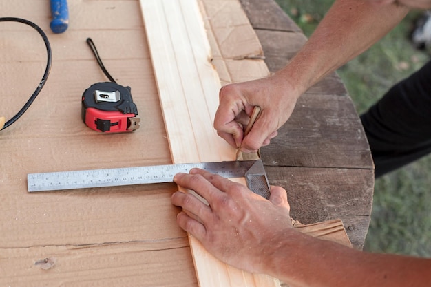 Las manos del carpintero toman medidas con una regla de metal en una tabla de madera y marcan la longitud con un lápiz