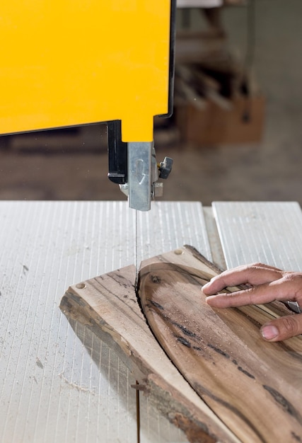 Manos de carpintero trabajando en una sierra de cinta con forma de madera para crear productos de interior