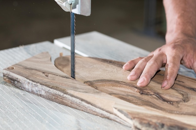 Manos de carpintero trabajando en una sierra de cinta con forma de madera para crear productos de interior
