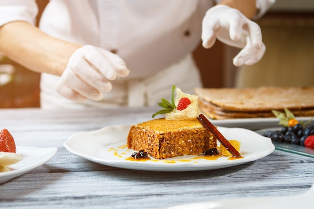 Manos cerca de plato con pastel. Pastel con decoración en plato. Pastel de miel y canela en rama. Receta tradicional y nuevo diseño.