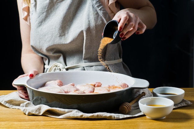 Las manos del chef asperjan especias alitas de pollo crudas.