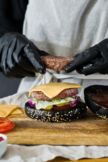 Foto las manos del chef cocinan la hamburguesa. el concepto de cocinar hamburguesa con queso negro. receta de hamburguesa casera.