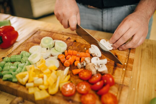 Manos de chef con cuchillo corta setas en primer plano de tablero de madera