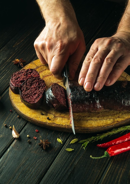 Foto las manos del chef con un cuchillo cortan salchichas de sangre en una tabla de corte de la cocina cocinando un plato nacional con especias y pimienta en casa en la cocina