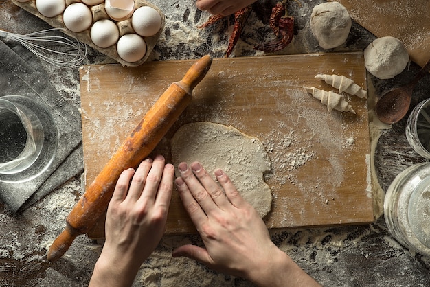 Foto las manos del chef están enrollando la masa sobre tabla de madera y harina de trigo