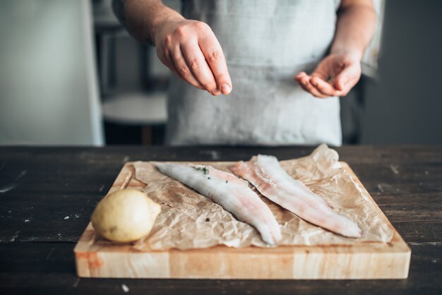 Manos de chef masculino salazón pescado crudo sobre tabla de cortar de madera cubierta con papel pergamino. Cocina de mariscos. Mariscos frescos