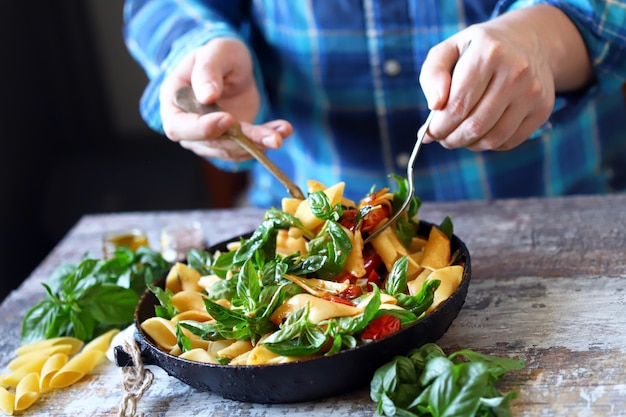 Las manos del chef mezclan la pasta con verduras y albahaca.