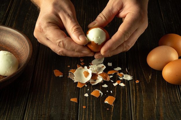 Las manos del chef pelan huevos hervidos para preparar un plato nacional en la mesa de la cocina Concepto de dieta saludable de huevos
