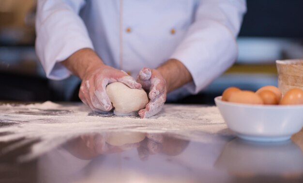 Manos del chef preparando la masa para pizza espolvoreada con harina en primer plano de la tabla