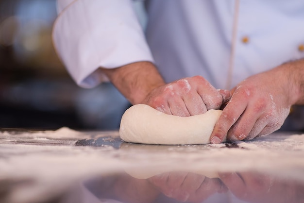 Manos del chef preparando la masa para pizza espolvoreada con harina en primer plano de la tabla