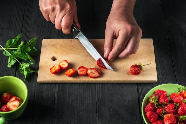 Las manos del chef de primer plano cortan fresas frescas en la tabla de cortar de la cocina del restaurante para hacer un refresco con menta. Cocinar postres dietéticos.