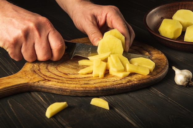 Las manos del chef de primer plano cortan patatas crudas con un cuchillo para preparar un plato nacional