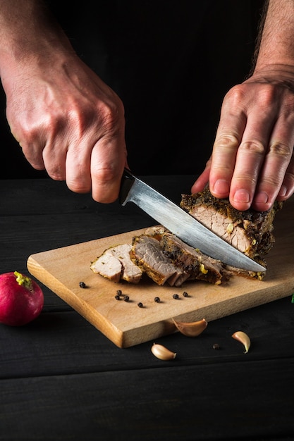 Manos del chef rebanar filete de ternera al horno con un cuchillo en la mesa de corte de madera. Concepto de proceso de preparación de alimentos de vista superior.