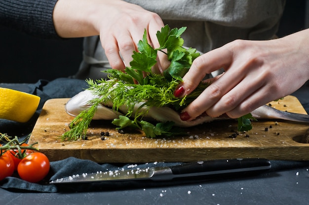 Las manos del chef rellenaron el pescado Dorado en una tabla de cortar de madera con perejil y cilantro.