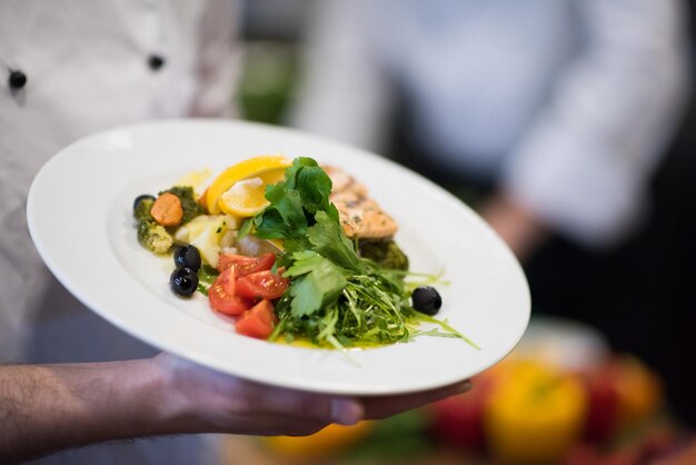 Manos de chef sosteniendo filete de pescado de salmón frito con verduras para cenar en la cocina de un restaurante