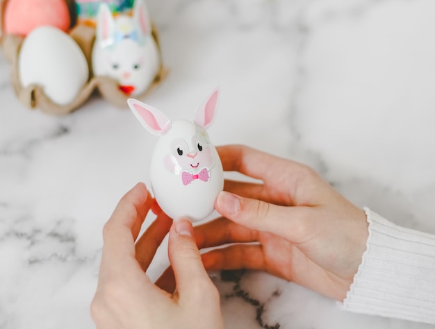 Manos de una chica caucásica sosteniendo un huevo de conejito de Pascua blanco hecho por sus propias manos