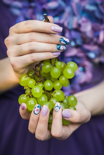 Las manos con clavos sostienen uvas verdes.