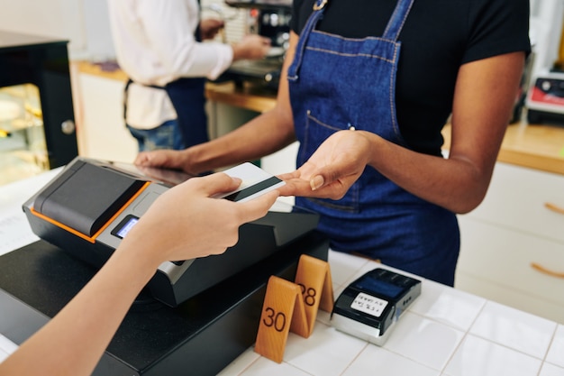 Foto manos del cliente dando tarjeta de crédito al cajero al pagar el pedido en el café