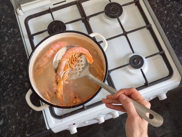 Manos cocinar grandes langostinos frescos en un tazón