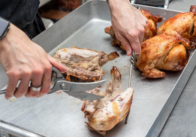 Las manos de un cocinero irreconocible cortando el pollo asado