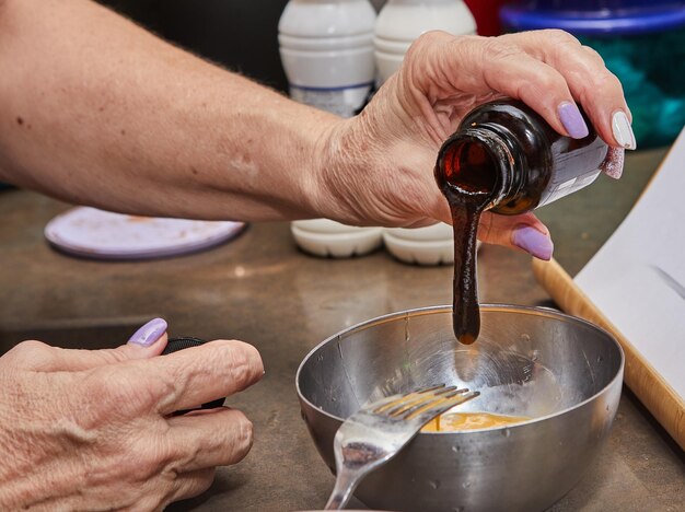 Las manos de los cocineros vertiendo jarabe en una taza con mezcla para cocinar en casa