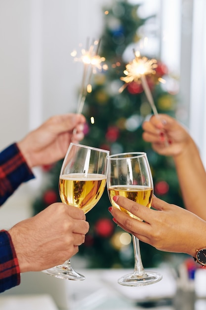 Manos de un colega de negocios brindando con copas de champán y luces de Bengala encendidas al celebrar la Navidad en la oficina