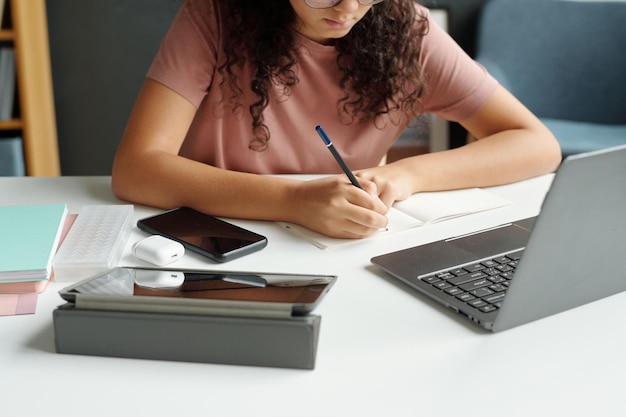 Manos de colegiala diligente tomando notas con lápiz en cuaderno