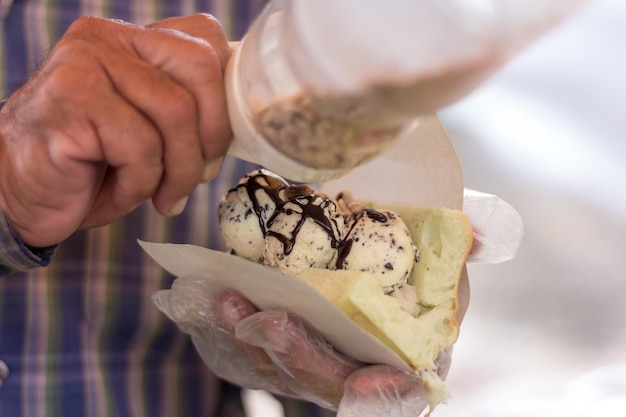 Las manos de un comerciante masculino recogen helado de chocolate de vainilla en pan y ingredientes