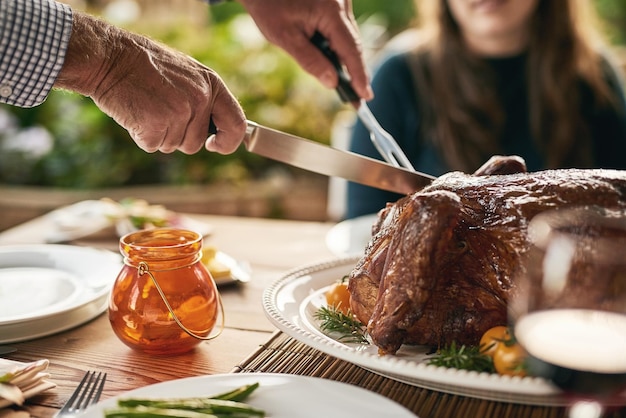 Manos de comida y pavo con la familia en una mesa para celebrar la tradición de acción de gracias y el almuerzo en un patio Mano de pollo y hombre tallando carne para compartir con amigos en la fiesta de navidad al aire libre