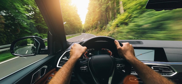 Manos del conductor del automóvil en el volante conduciendo un automóvil rápido en el día de la primavera en una carretera rural divirtiéndose conduciendo la carretera vacía en el viaje POV vista en primera persona