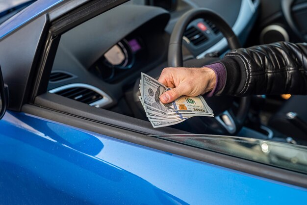 Manos de conductor de coche masculino sosteniendo nuevos billetes de un dólar en el medio en el interior del coche. Concepto de negocio.