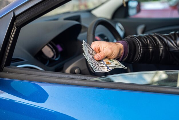 Manos de conductor de coche masculino sosteniendo nuevos billetes de dólar en el medio en el interior del coche Concepto de negocio