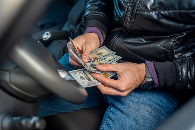 Manos de conductor de coche masculino sosteniendo nuevos billetes de dólar en el medio en el interior del coche Concepto de negocio