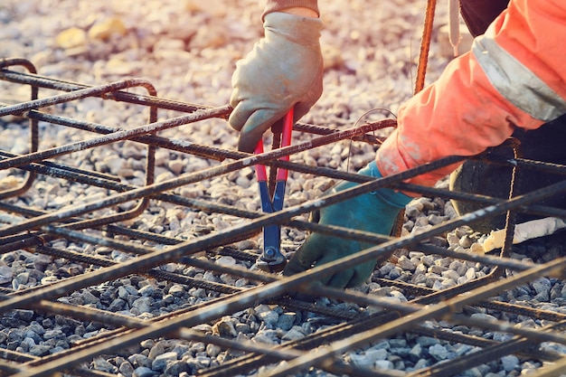 Manos del constructor que fijan las barras de refuerzo de acero Fijador de acero que ensambla la jaula de refuerzo