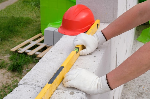 Manos de constructores en un guante y un nivel de construcción para comprobar la pared al aire libre