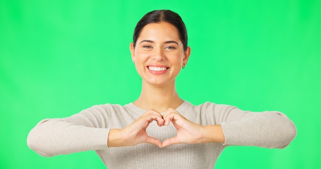 Manos de corazón y cara de mujer feliz en estudio de pantalla verde y fondo de color Retrato de forma de dedo de modelo femenino y amor por el apoyo gracias y emoji signo de amabilidad cuidado e icono de paz