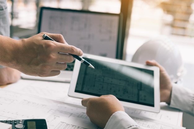 Manos cortadas de arquitectos usando tableta digital sobre planos en el escritorio