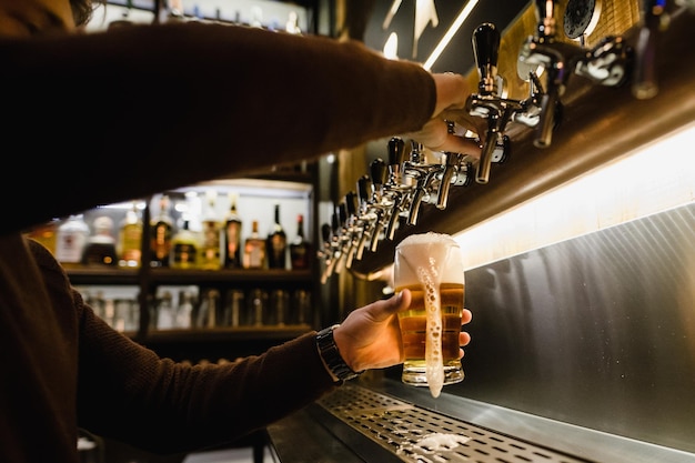 Manos cortadas del camarero llenando el vaso de cerveza en el bar