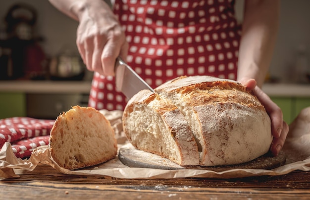 Manos cortadas con un cuchillo pan fresco natural casero con una corteza dorada sobre fondo de madera Productos de panadería para hornear