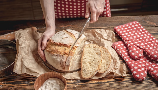 Manos cortadas con un cuchillo pan fresco natural casero con una corteza dorada sobre fondo de madera Productos de panadería para hornear