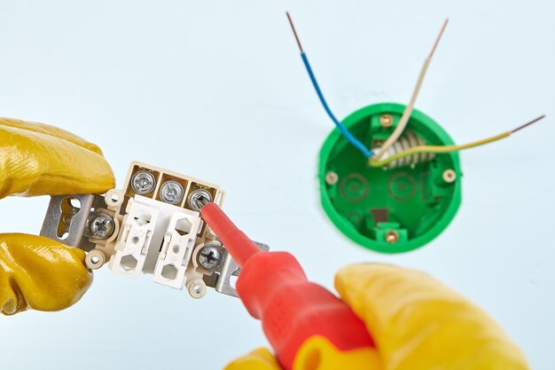 Foto manos cortadas de un electricista trabajando sobre un enchufe eléctrico en la pared