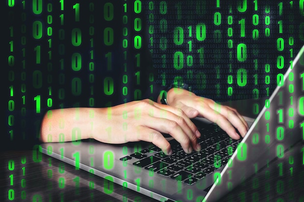 Las manos cortadas de un hacker informático hackeando una computadora portátil con números binarios