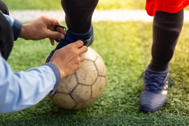 Foto manos cortadas de un hombre atando el cordón de un jugador en una pelota de fútbol