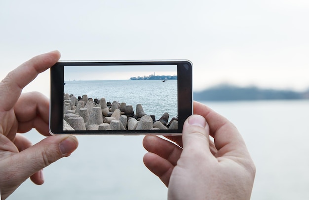 Manos cortadas de un hombre fotografiando el mar con un teléfono móvil