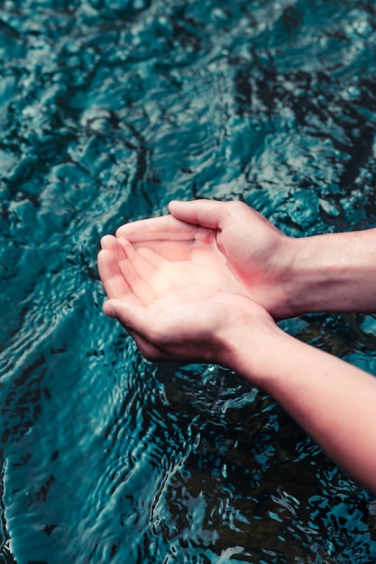 Manos cortadas de un hombre sosteniendo agua de un río que fluye