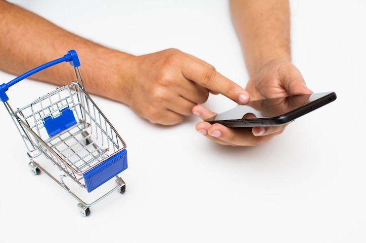 Foto manos cortadas de un hombre usando un teléfono con un pequeño carrito de compras sobre un fondo blanco