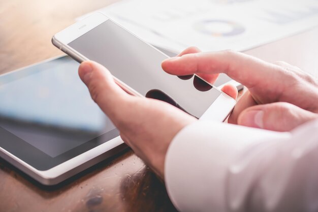 Manos cortadas de un hombre usando un teléfono por una tableta digital en el escritorio