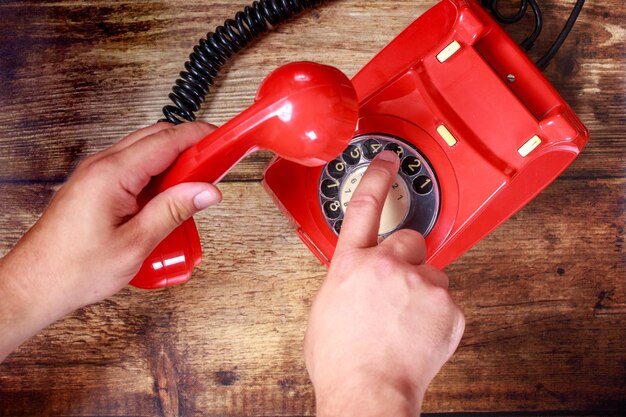 Foto manos cortadas marcando en el teléfono rotativo rojo en la mesa